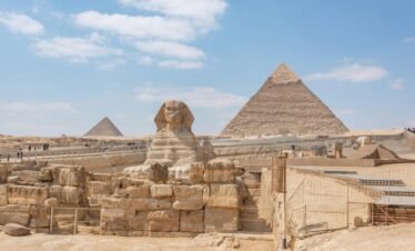 Iconic view of the Great Sphinx and Giza Pyramids in Egypt under a clear blue sky.