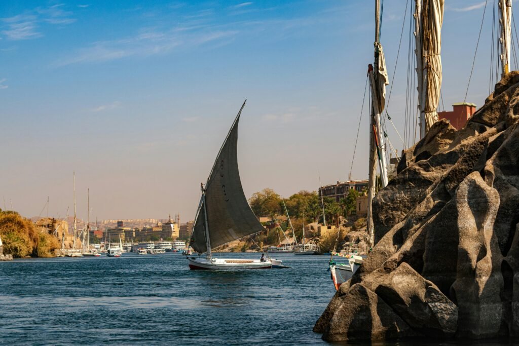 A traditional sailboat glides on the scenic Nile River near Aswan, Egypt, showcasing a tranquil landscape.