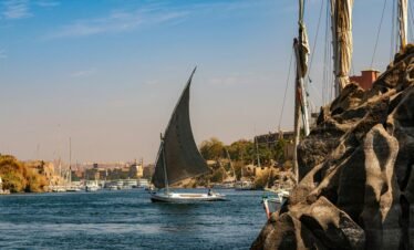 A traditional sailboat glides on the scenic Nile River near Aswan, Egypt, showcasing a tranquil landscape.